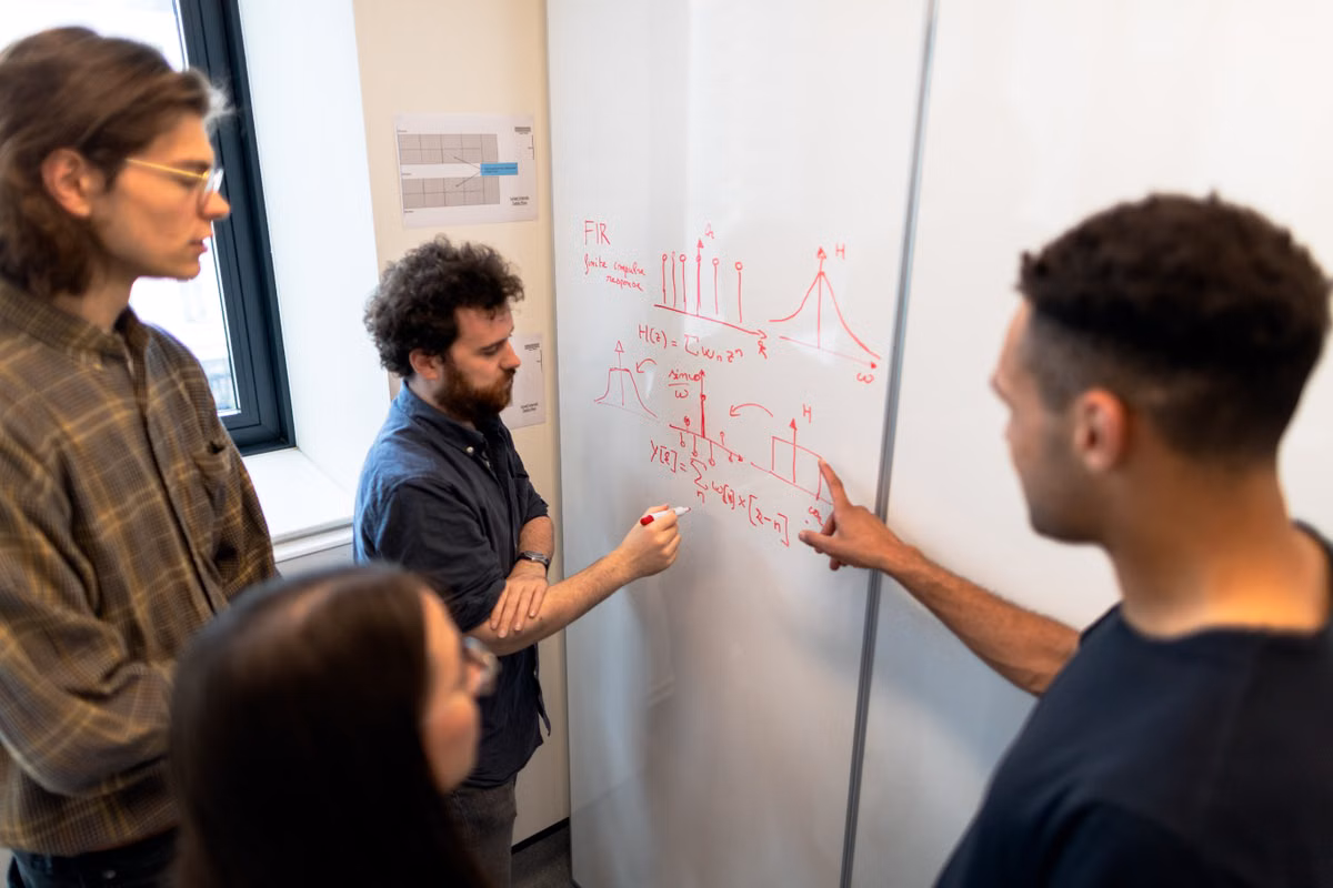 Engineers discussing technical work at a whiteboard during a team meeting